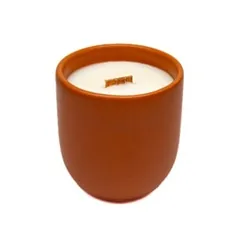 A natural scented candle in a burnt orange matt ceramic vessel, custom-made for the product line of a European brand